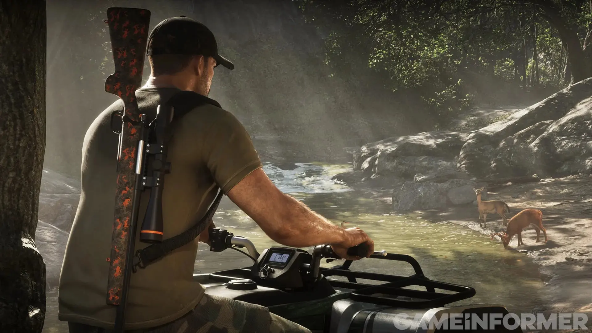 A man in a cap with a rifle slung on his back rides an ATV beside a creek where two deer are drinking among the rocks.