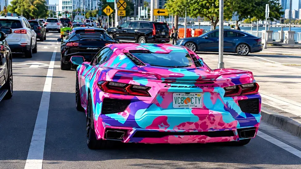 Un deportivo decorado con manchas rosas, azules y moradas y una matrícula de Florida, parado en el tráfico de Miami junto a la bahía.