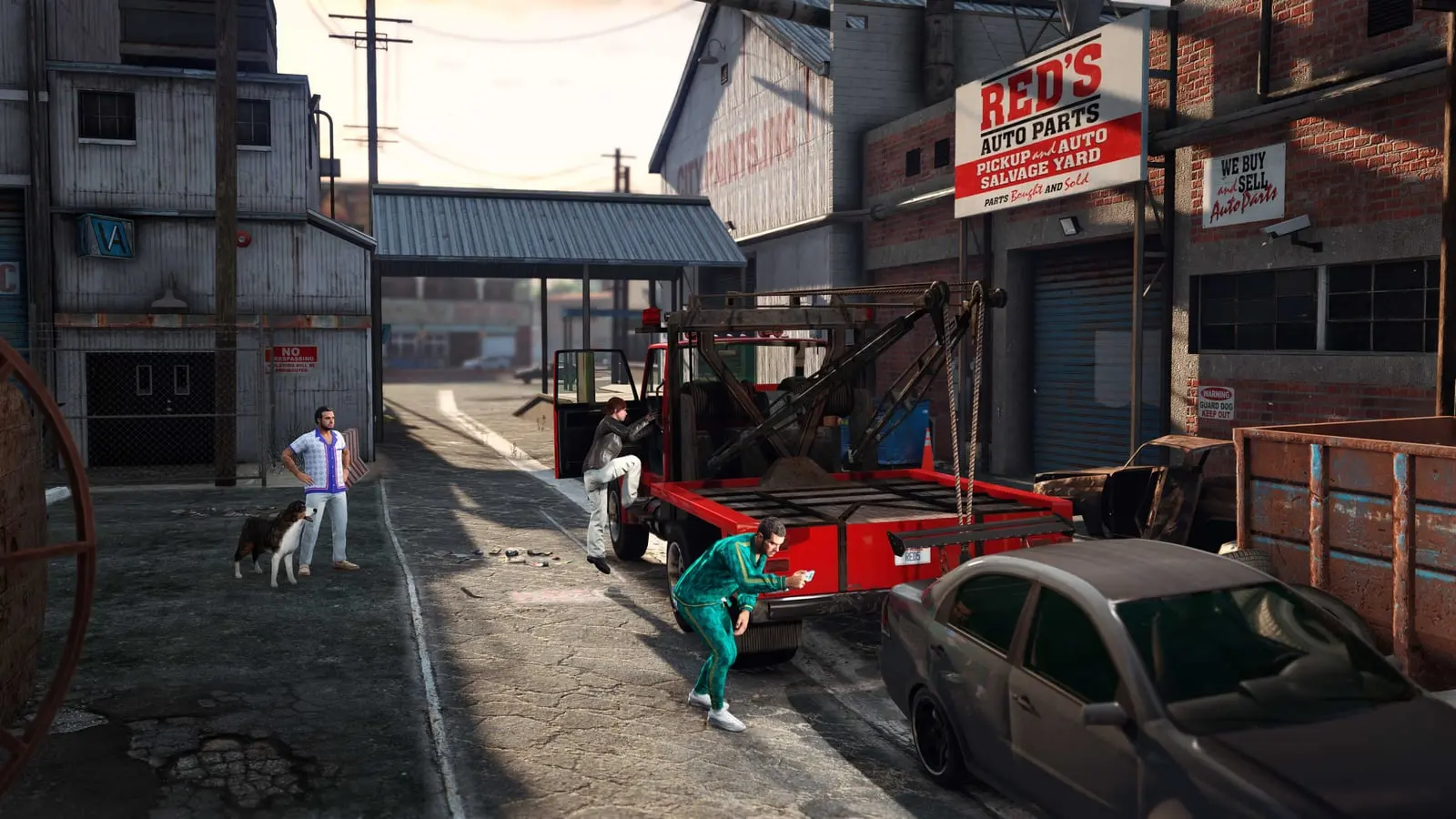 Entrada del desguace Red's Auto Parts con coches aparcados, un perro y un empleado junto al taller.