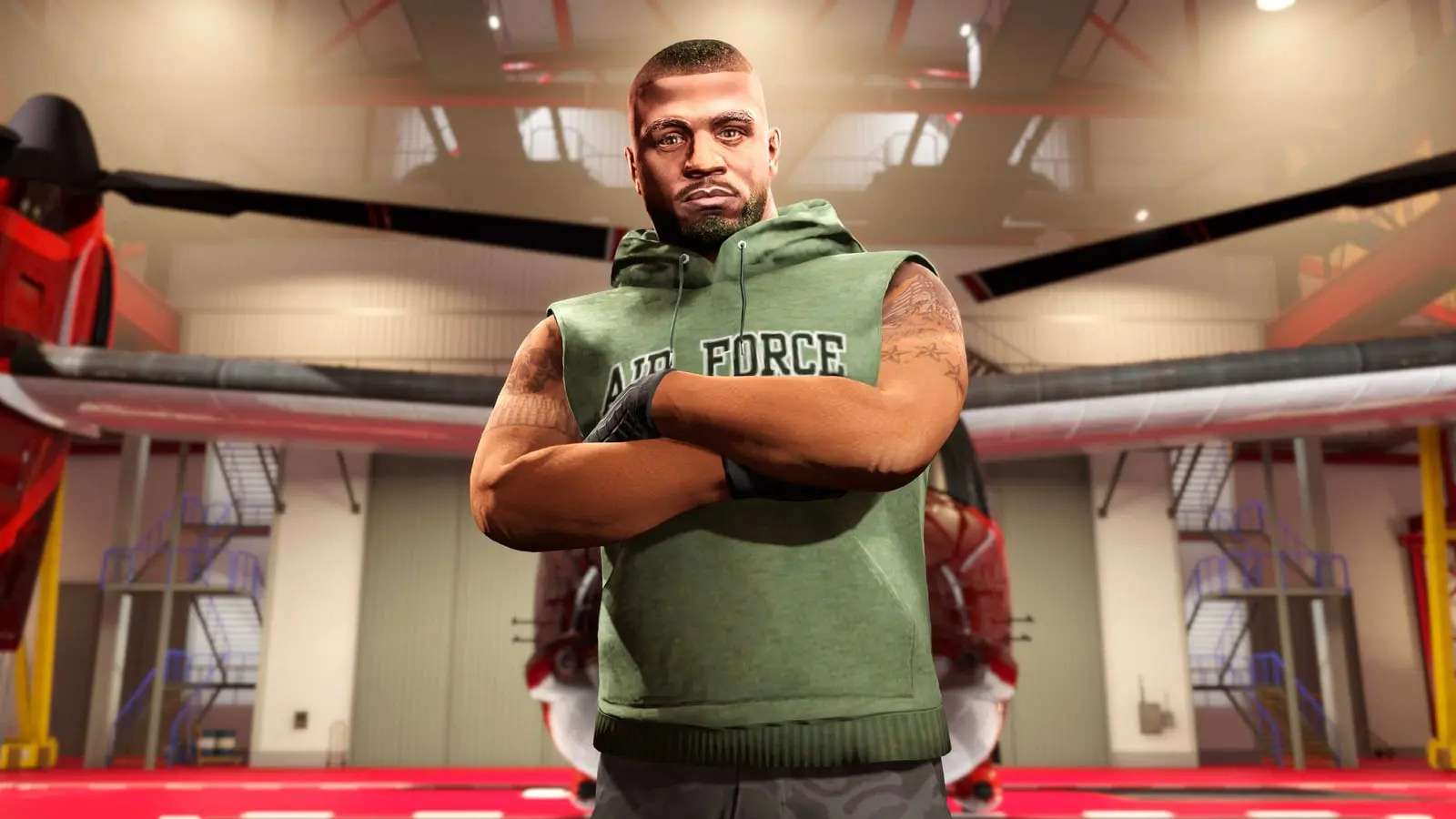 A man in a sleeveless military tee with arms crossed inside a hangar.