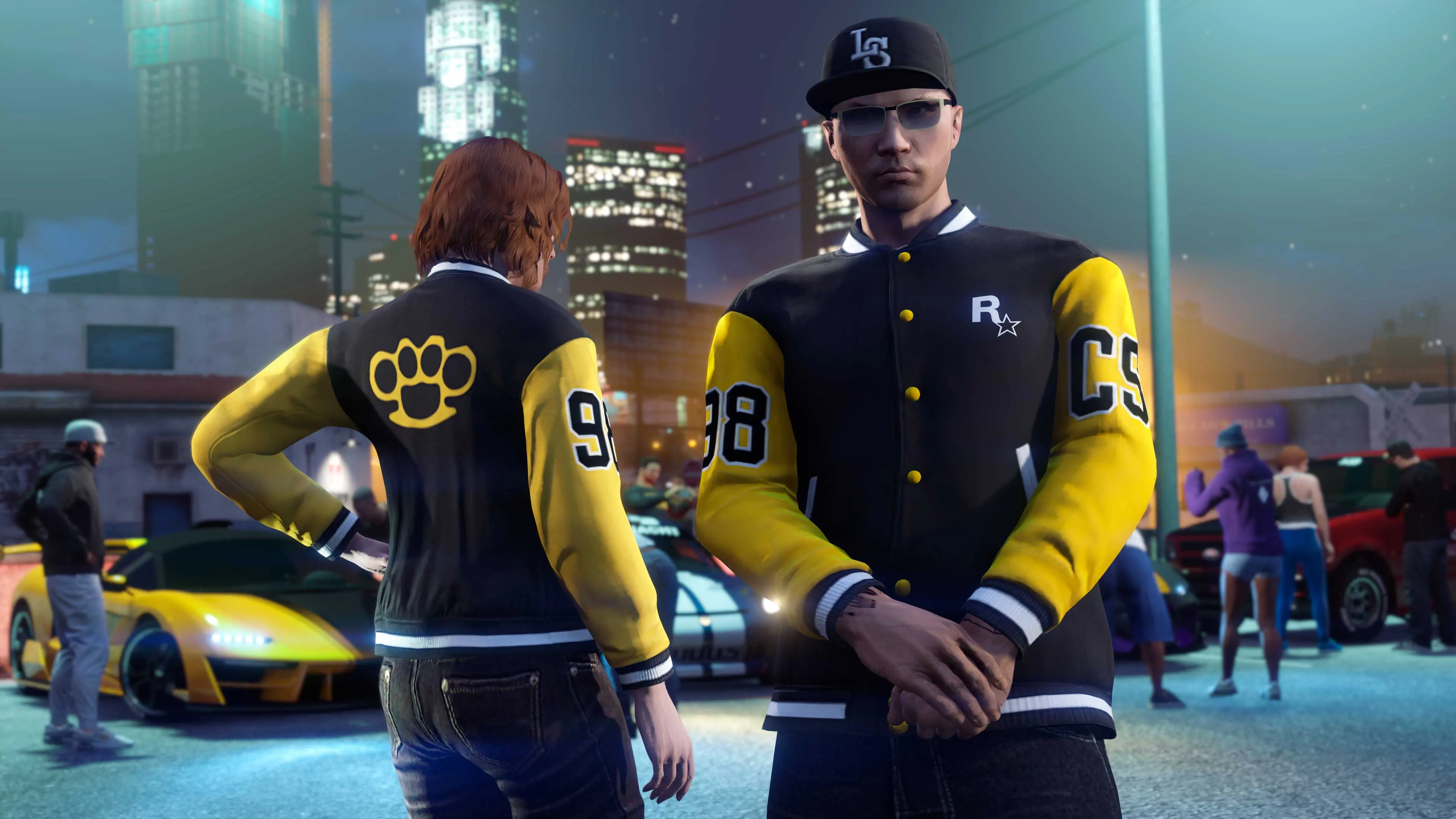 Dos personajes de GTA Online con la chaqueta de la Community Series en una quedada de coches.
