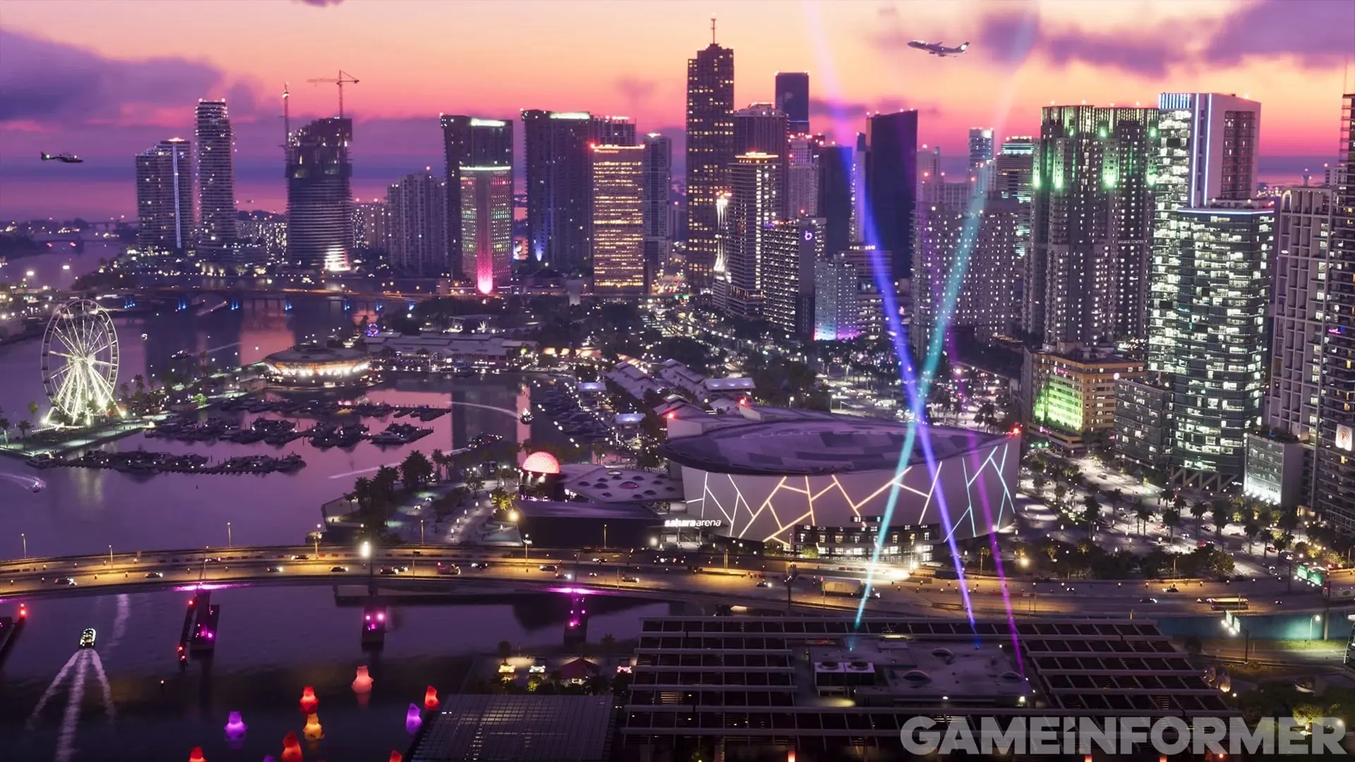 The Vice City skyline at dusk with lit towers, a Ferris wheel, an arena by the bay and searchlights pointing into a purple sky.