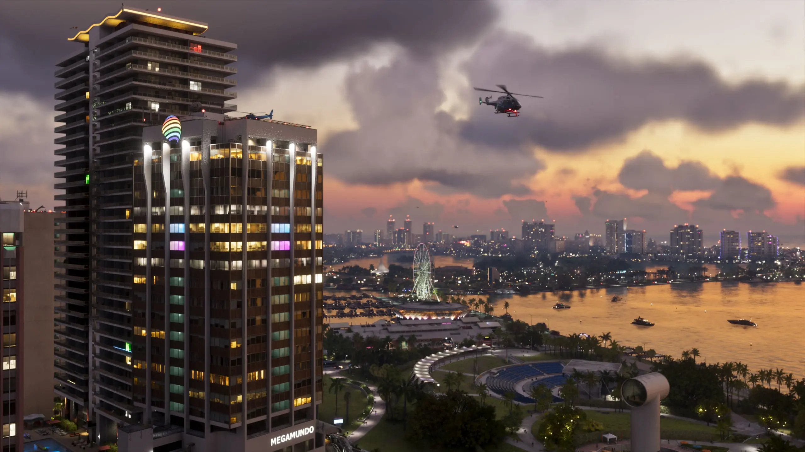 Vice City al atardecer en GTA VI: un rascacielos iluminado en primer plano, un helicóptero sobre la bahía y una noria al fondo.
