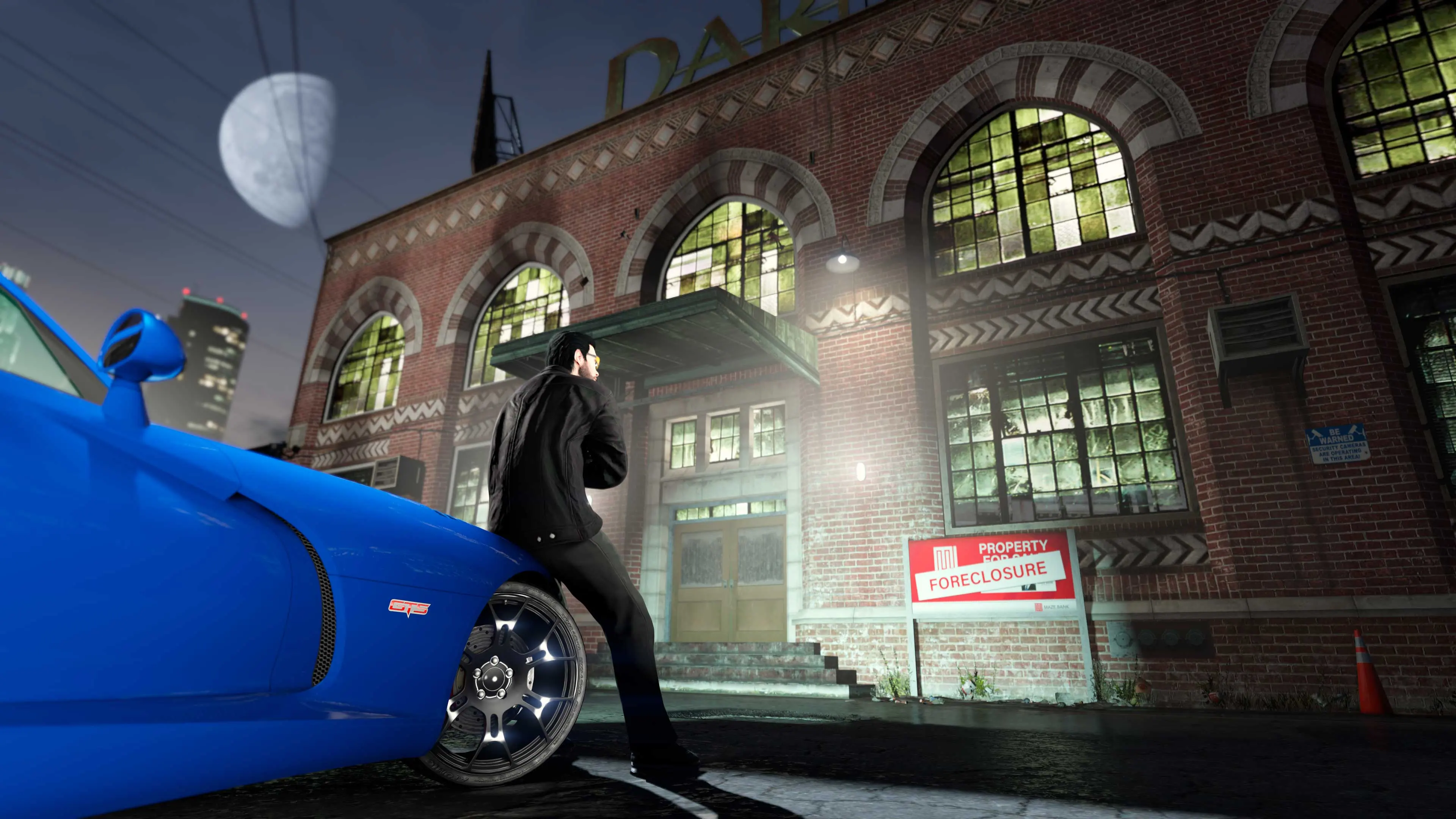Un personaje de GTA Online apoyado en un coche mira hacia la fábrica textil Darnell Bros.